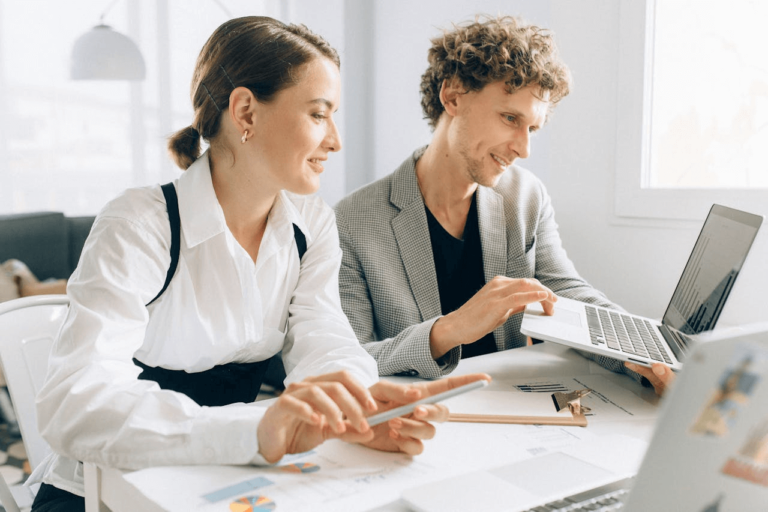 Een man en een vrouw werken samen aan een bureau met laptops en documenten.